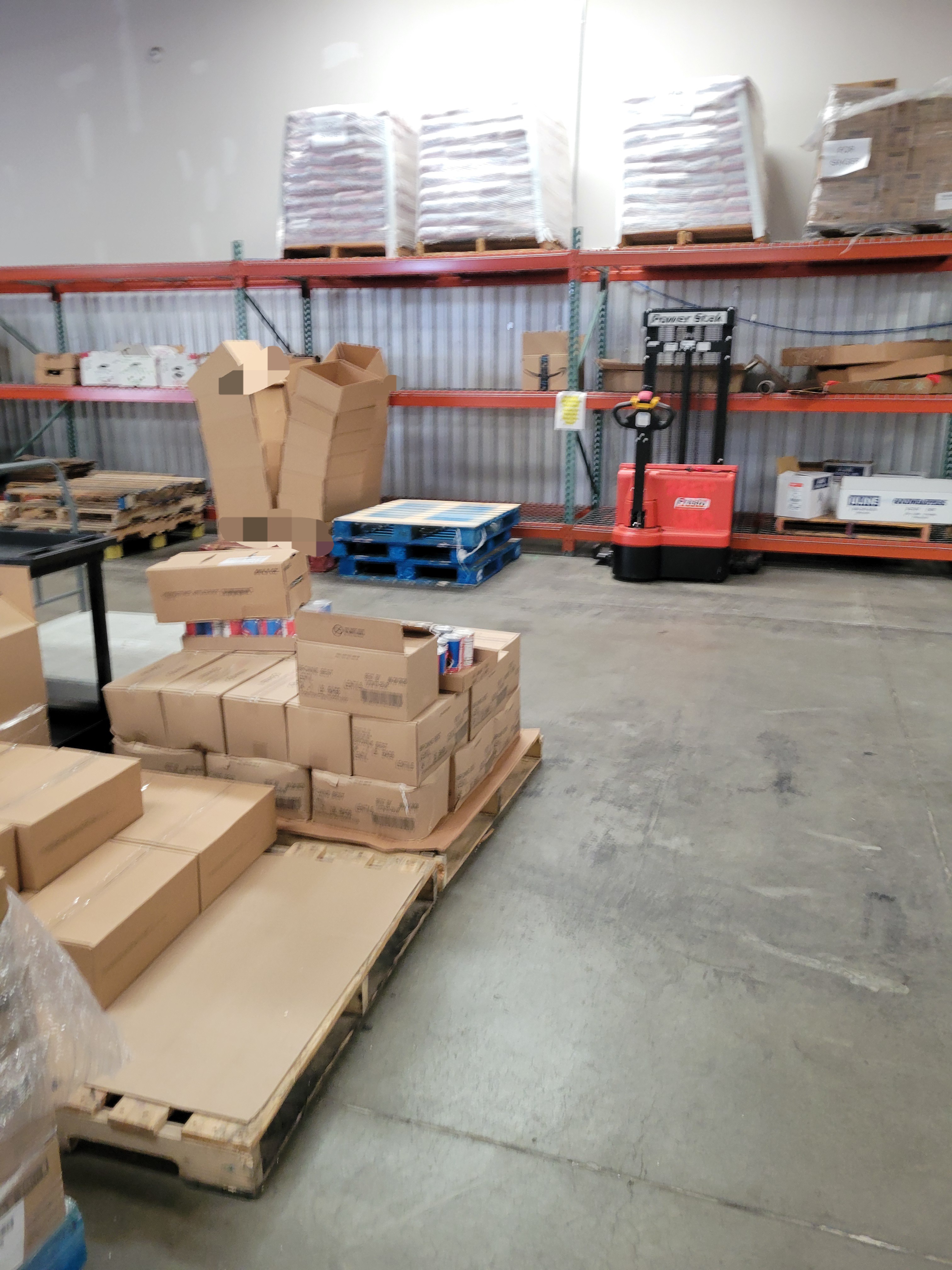 Warehouse filled with pallets, shelves and a electric pallet stacker.